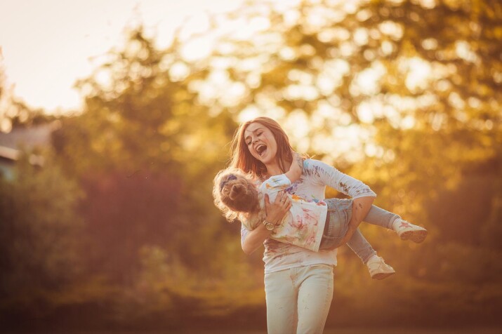 A joyful woman lifts a smiling child outdoors at sunset.