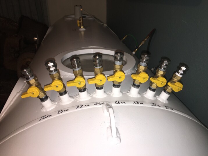 A row of yellow valve handles on a white industrial tank.