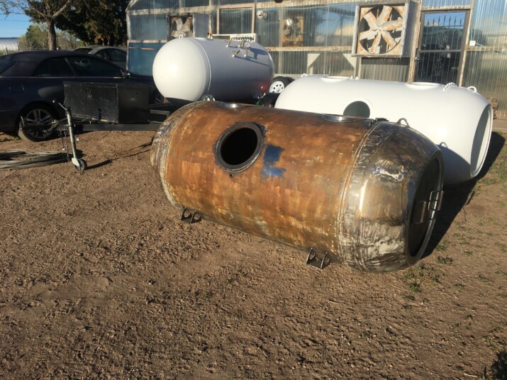A large rusty cylindrical metal tank lying on the ground outdoors.