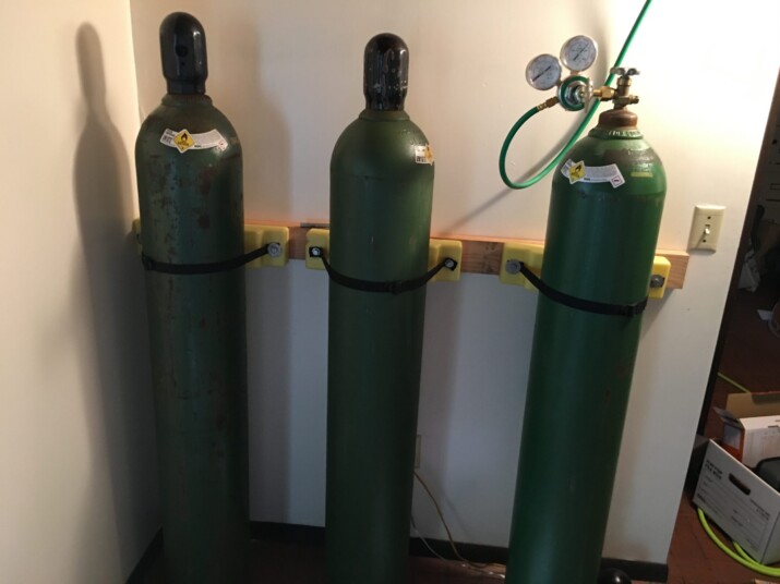 Three tall green gas cylinders standing upright indoors.