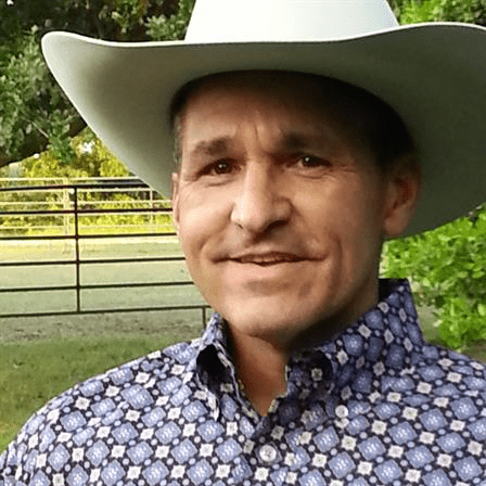 Man wearing a white cowboy hat and patterned shirt outdoors.
