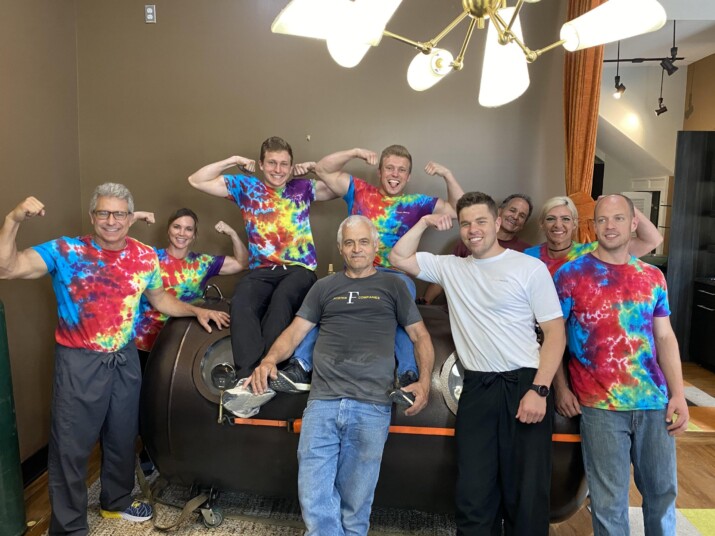 A group of people posing together in colorful tie-dye shirts indoors.